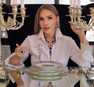 A young female founder sketching jewelry designs at a desk, surrounded by gemstones, tools, and early prototypes of the Azzallure collection.