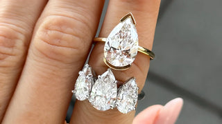 Hand showcasing multiple pear-shaped diamond rings including a bold solitaire teardrop diamond in yellow gold and a cluster setting