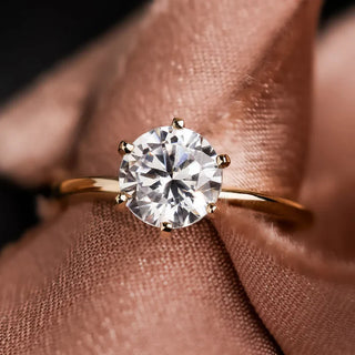 Round diamond solitaire ring with a thin yellow gold band, displayed over soft silk fabric.