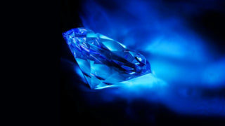Close up side view of a faceted diamond glowing vivid electric blue under ultraviolet light, illustrating the fluorescence effect in diamonds against a dark background.