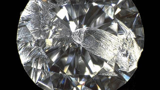 Close-up of a diamond under magnification showing surface clarity, with a metal tool nearby, illustrating the concept of diamond hardness and scratch resistance.