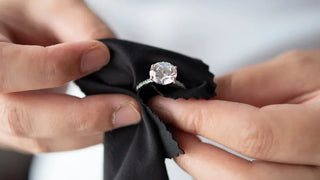 A diamond ring soaking in a bowl of warm soapy water next to a soft toothbrush and microfiber cloth—showcasing a simple and fun at-home cleaning routine to restore its sparkle.