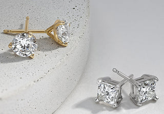 Pair of classic round diamond stud earrings displayed on a white velvet jewelry box