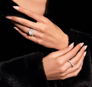 Elegant hands wearing a classic diamond engagement ring and matching band styled against a black textured outfit