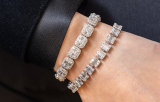 Close-up of a wrist adorned with two luxury tennis diamond bracelets featuring emerald-cut diamonds in intricate halo and prong settings, styled with an elegant black satin sleeve.