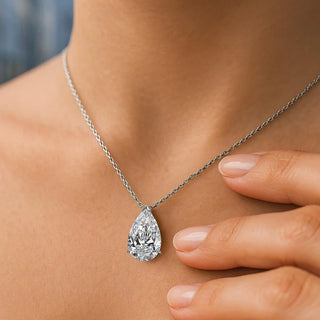 Woman wearing an elegant pear cut moissanite pendant necklace on a delicate silver chain, styled with a soft beige satin camisole, showcasing a minimalist and refined look.