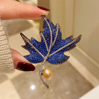 Maple leaf brooch made of copper and silver, set with green, blue, and red gemstones.