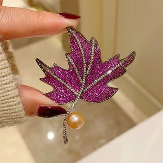 Maple leaf brooch made of copper and silver, set with green, blue, and red gemstones.