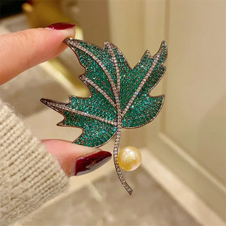 Maple leaf brooch made of copper and silver, set with green, blue, and red gemstones.